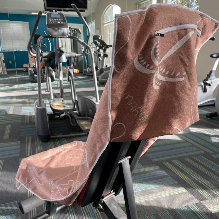 A gym towel that blends warm, earthy colours and artistic white detailing with a bright, contemporary gym setting, creating a visually appealing scene