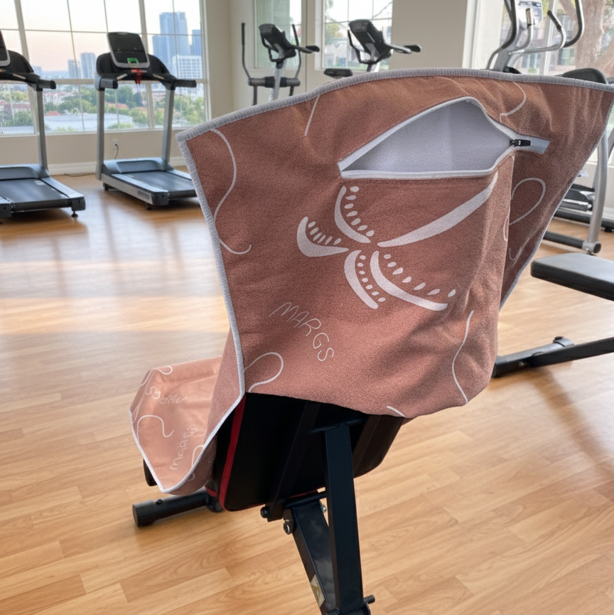 A flowing white lines and curved shapes, giving the towel a relaxed, organic feel. In contrast, the background showcases structured gym equipment and straight lines, emphasizing balance between softness and strength.