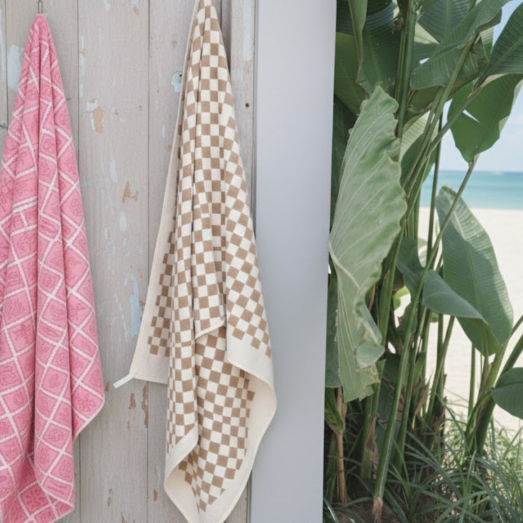 Pink and checkered towels hanging on a wooden post with a beach view in the background.