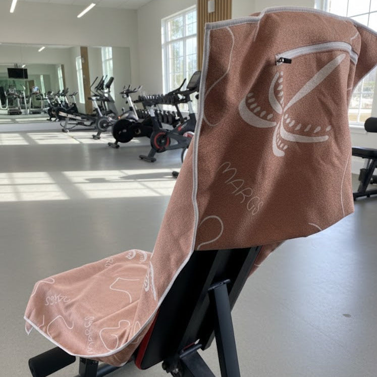 A minimalist abstract pattern in white, the towel’s design feels contemporary and artistic standing out among ellipticals, bikes, and mirrors creates a clean, professional fitness setting.